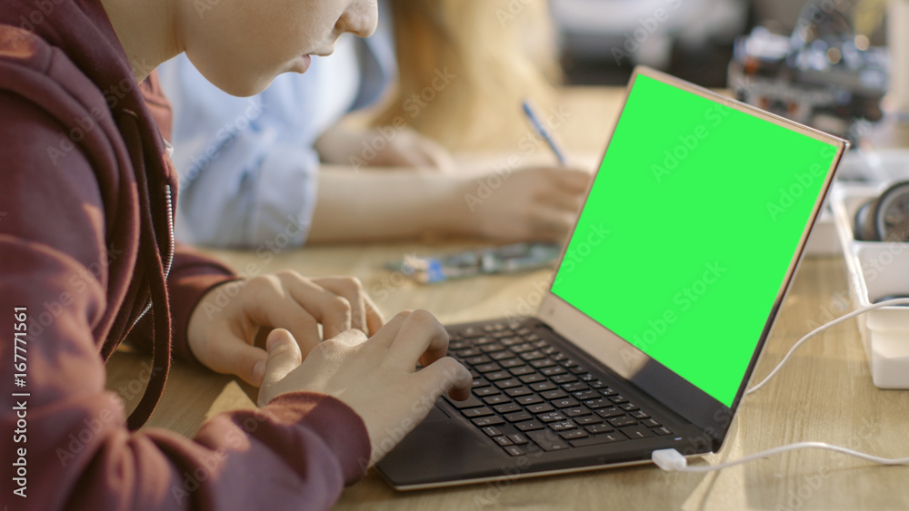 聪明的小男孩在他的计算机科学课上用一台带绿色屏幕的笔记本电脑工作。