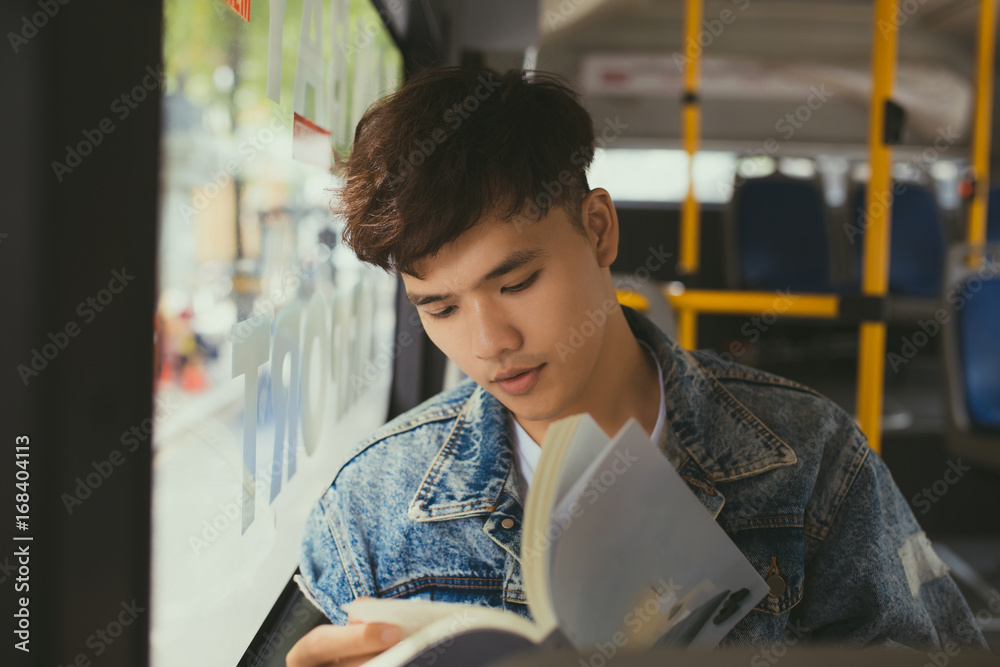 一个年轻人坐在城市公交车上看书。