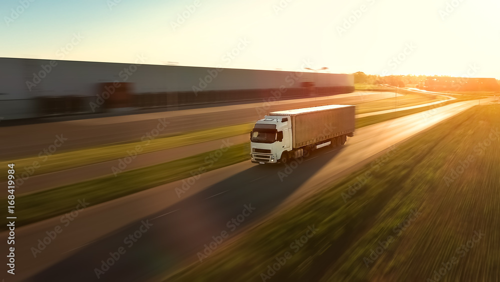 白色半卡车和货运拖车在高速公路上行驶的鸟瞰图。背景是仓库
