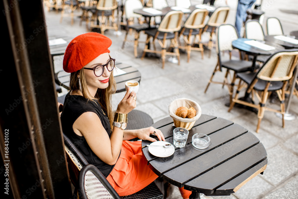 戴着红色贝雷帽的年轻时尚女性，在门口享用法式早餐，配咖啡和羊角面包