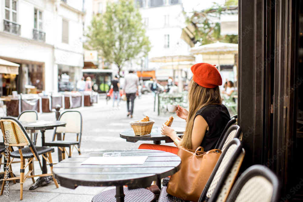 戴着红色贝雷帽的年轻时尚女性，在餐厅享用法式早餐，配咖啡和羊角面包