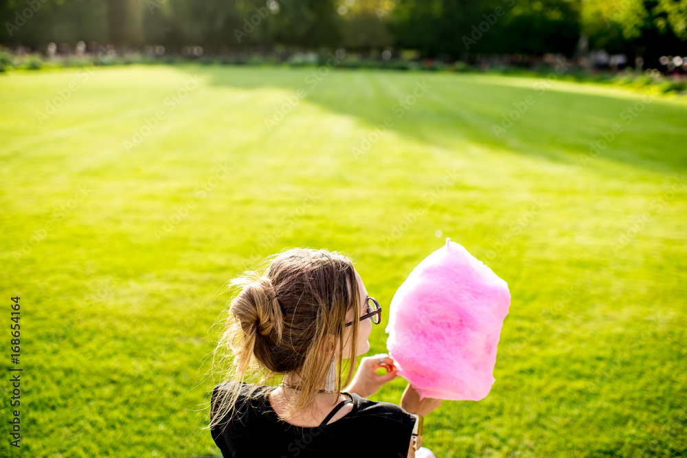 Young woman with pink cotton candy sitting back outdoors at the park