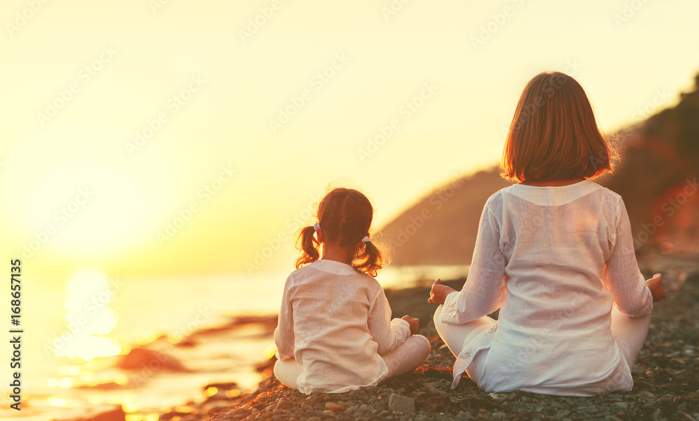 快乐的家庭母亲和孩子做瑜伽，在海滩上以莲花姿势冥想
