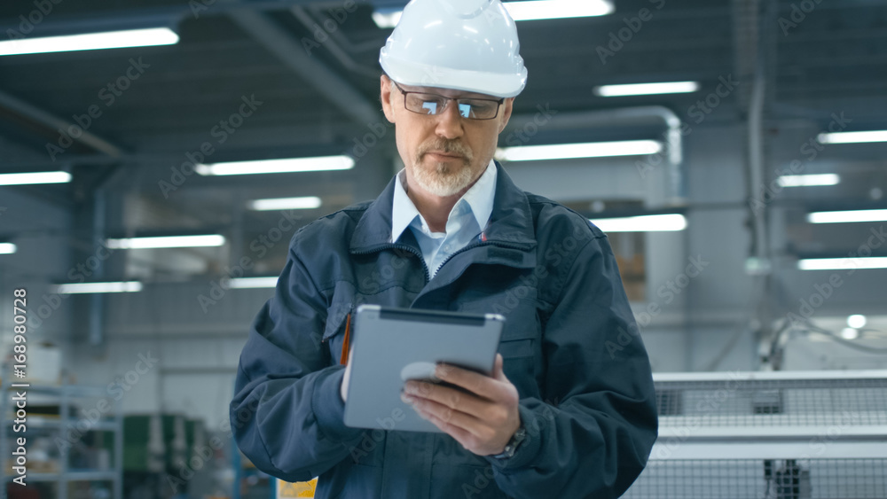 安全帽公司的高级工程师正在工厂里使用平板电脑。