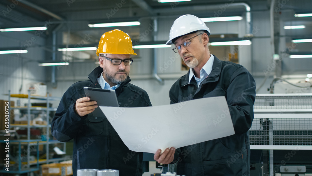 两名工程师在工厂检查平板电脑上的信息时讨论蓝图。