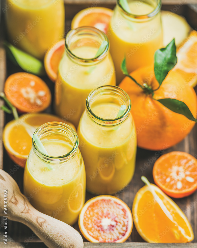 健康的黄色奶昔，配柑橘类水果和生姜，装在灰色混凝土坝上的木托盘里