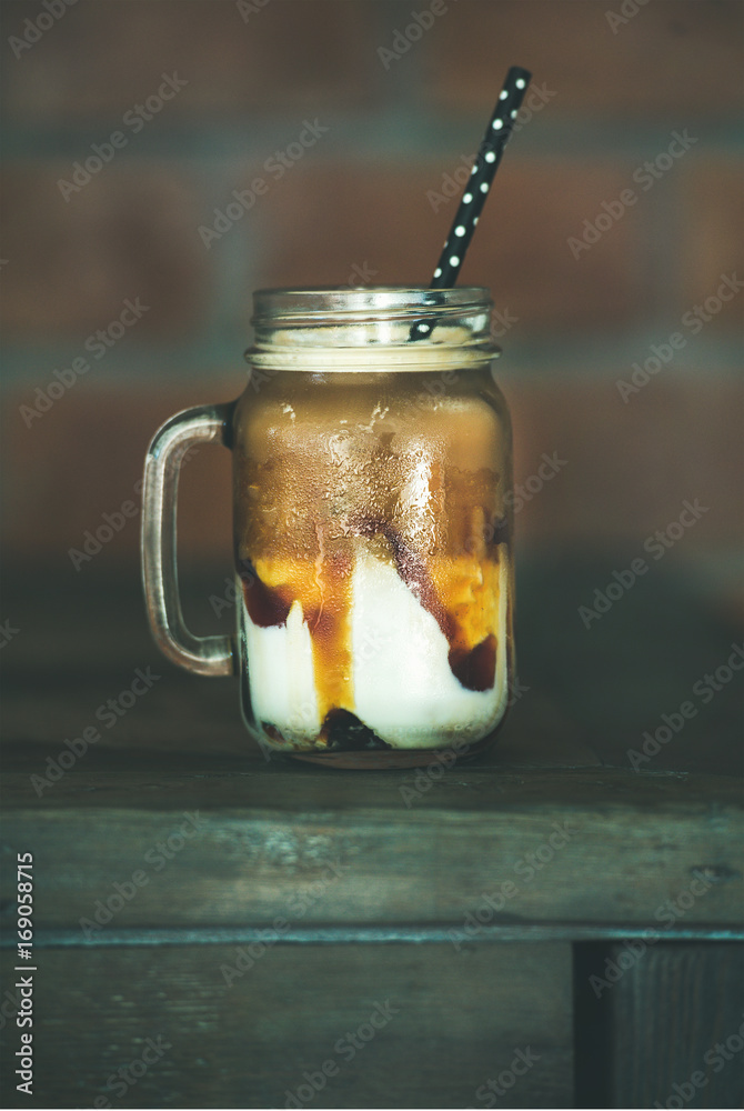 玻璃罐中的冰焦糖macciato咖啡配牛奶，深色木桌上有吸管，选择性聚焦