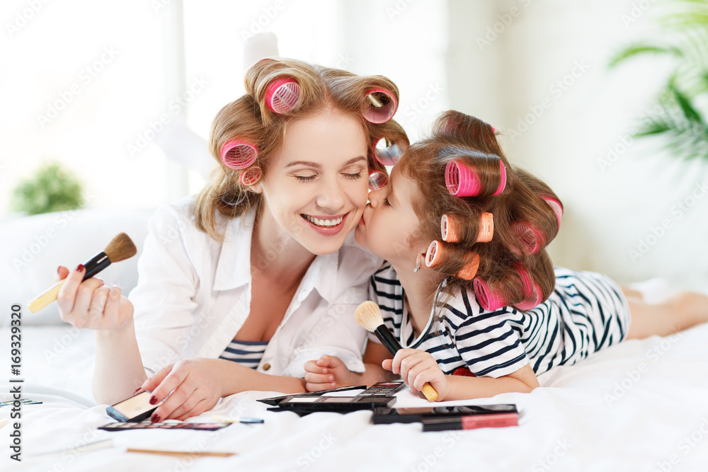 Mother and baby daughter in curlers  doing makeup on bed