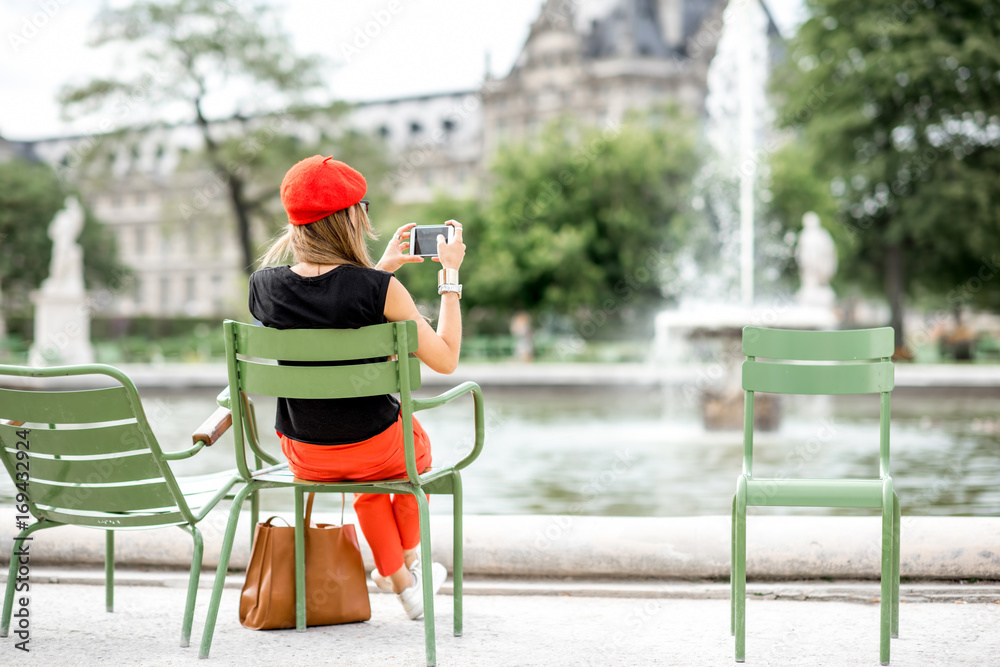 年轻时尚的女士，戴着红色帽子，穿着裤子，坐在巴黎杜乐丽花园著名的绿色椅子上