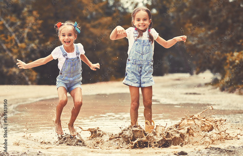 快乐有趣的双胞胎姐妹一个接一个地穿着橡胶靴在水坑上跳，大笑不止。