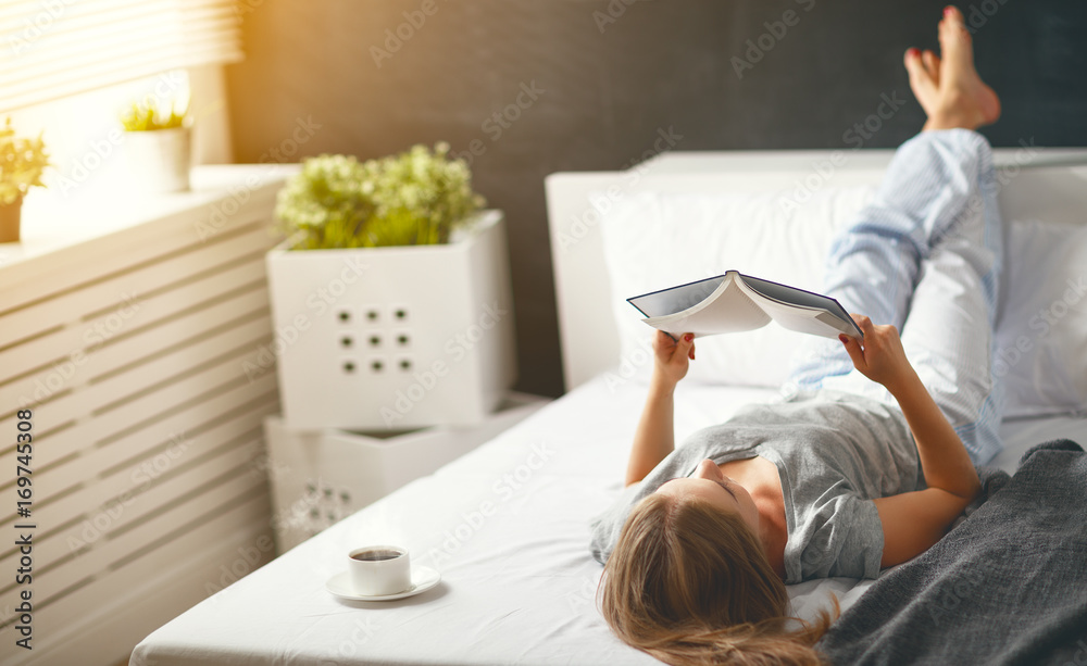 快乐的年轻女人在床上看书喝咖啡
