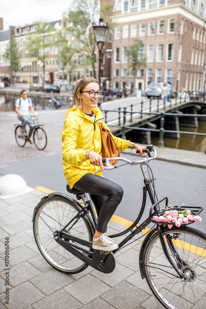 阿姆斯特丹市一名身穿黄色雨衣、带着袋子和鲜花骑自行车的年轻女子