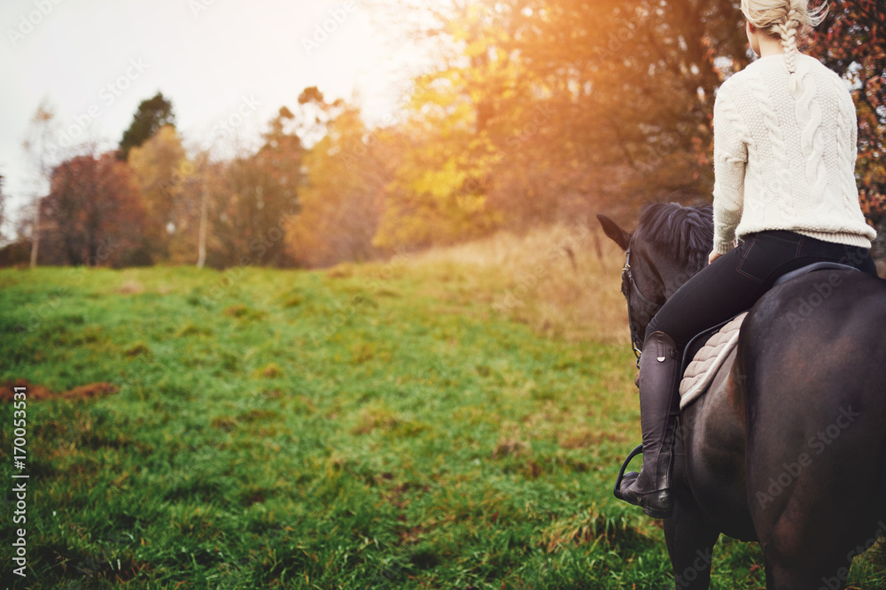 年轻女子牵着栗色的马穿过秋天的牧场