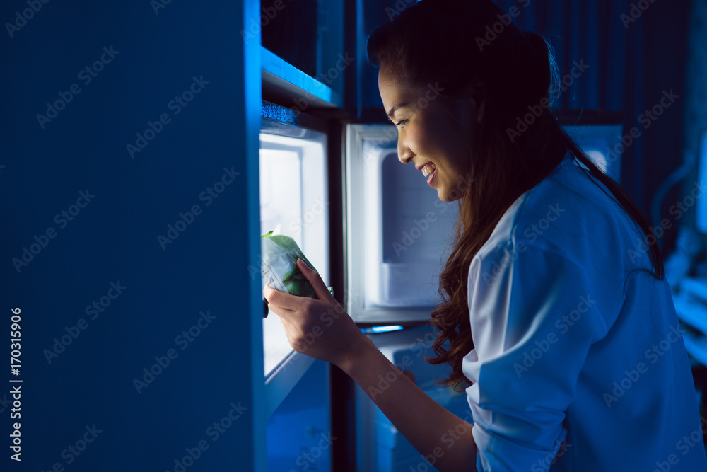 亚洲女性打开冰箱，晚上吃甜点。