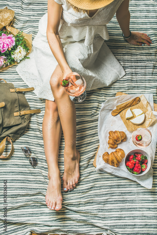 法式浪漫野餐场景。穿着棉质连衣裙，戴着帽子的女人，手里拿着一杯葡萄酒和草莓