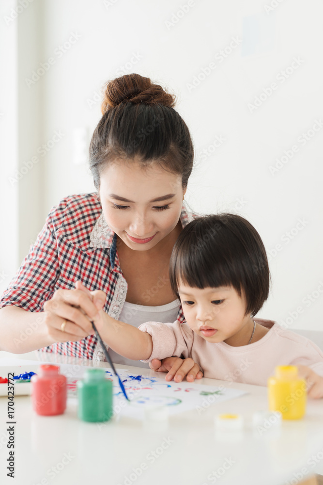 幸福的家庭，母亲和女儿一起画画。亚洲妇女帮助她的小女儿。