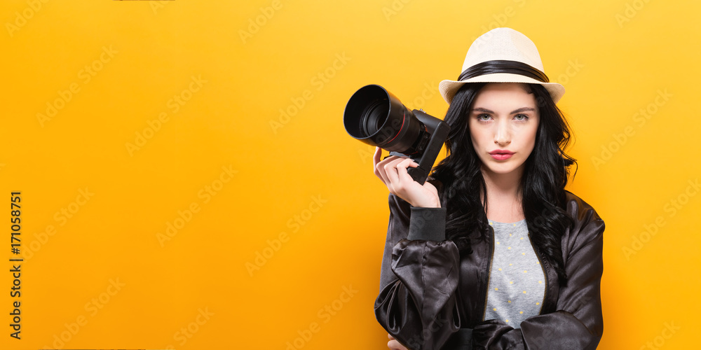 黄色背景下拿着相机的年轻女子