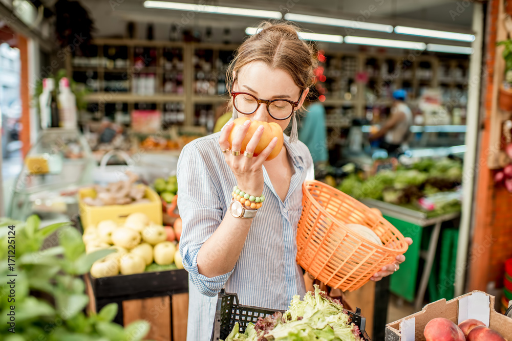 法国菜市场上，一名年轻女子拿着篮子站着挑选新鲜番茄