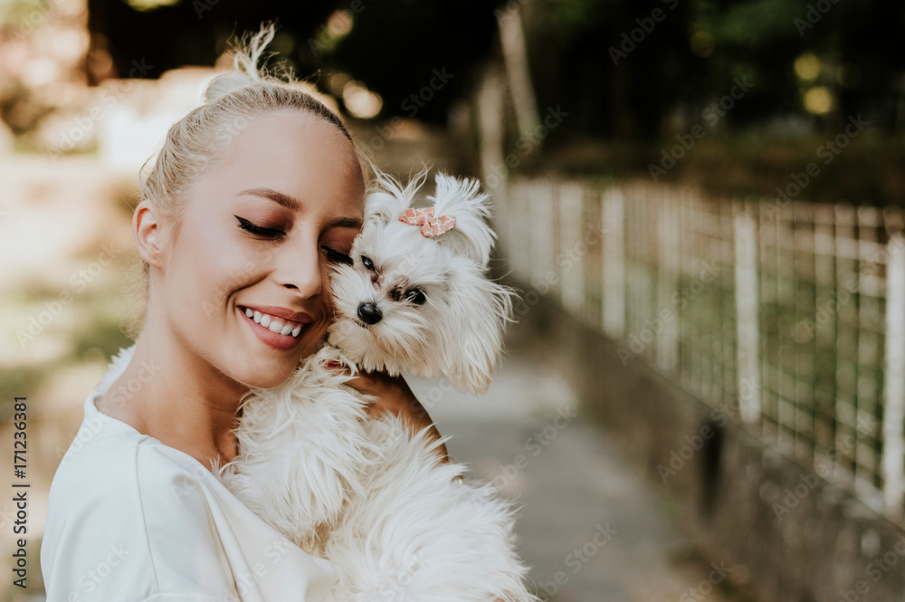 Pretty woman holding a cute, small maltese dog.