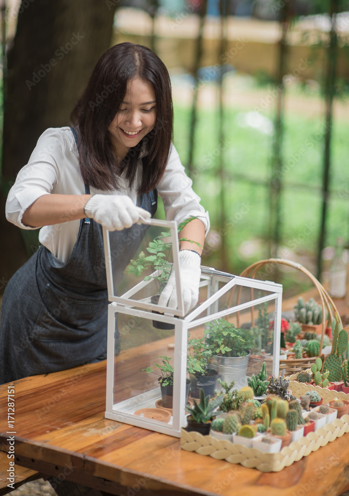 Happy young Asian woman putting plant to mini glass house