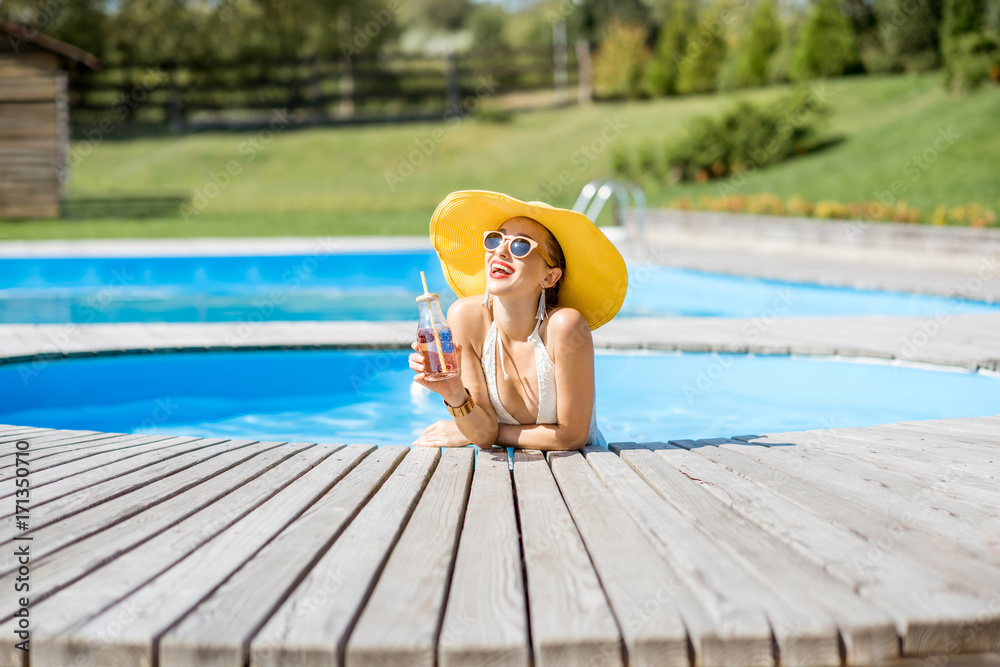 Young woman in swimsuit with big yellow sunhat relaxing with a bottle of fresh drink sitting on the 