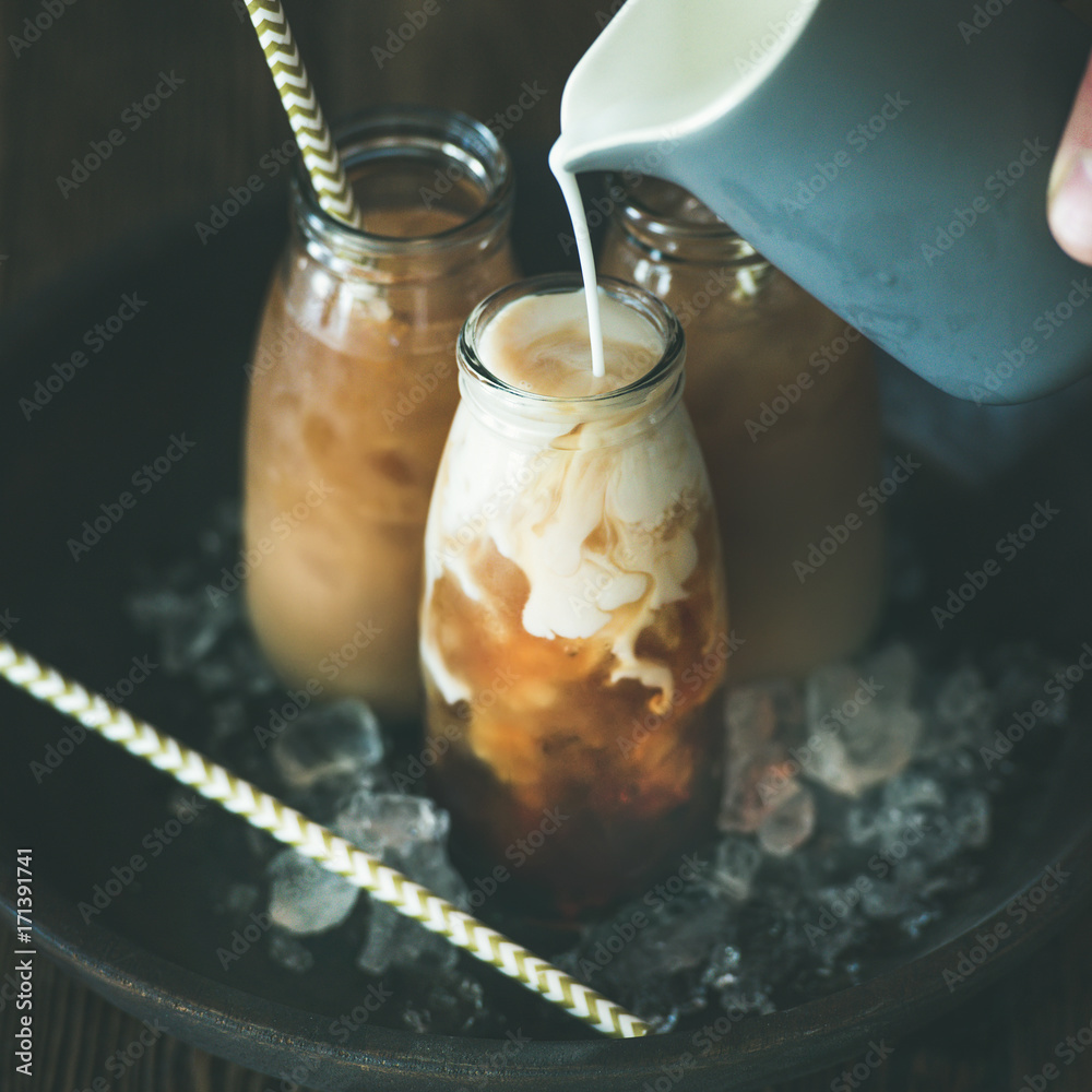 清爽的夏日饮品。装在玻璃瓶里的冷泰国冰茶，牛奶从白色罐子里倒在pla上