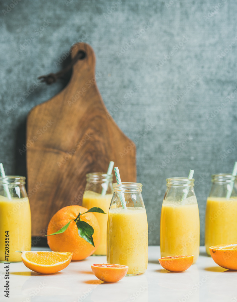 健康的黄色奶昔，装在浅色大理石桌子、木板上的瓶子里，有柑橘类水果和生姜