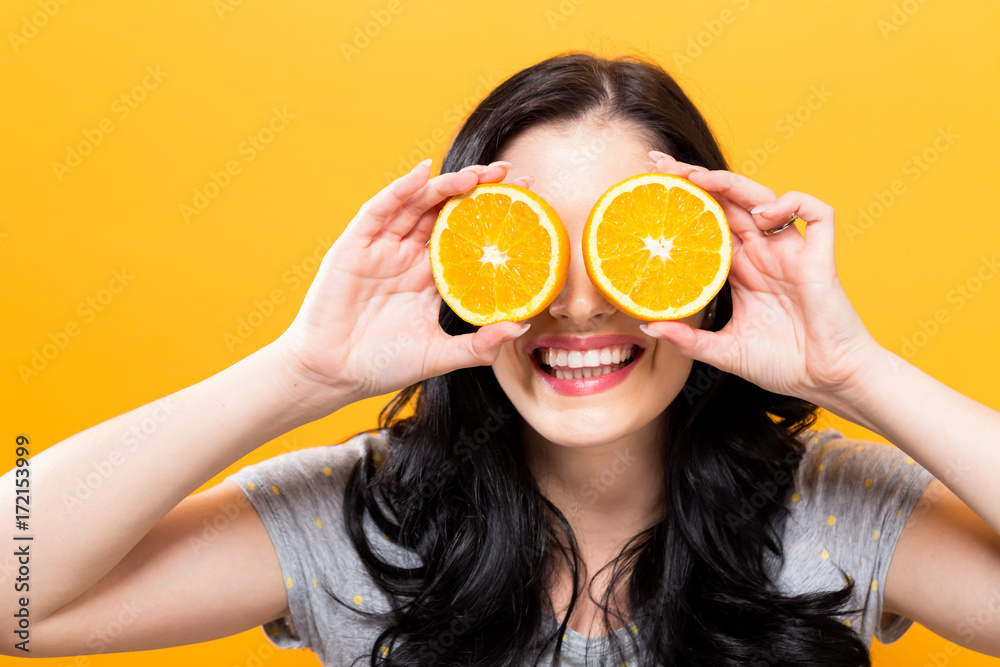 黄色背景下拿着橘子的快乐年轻女人