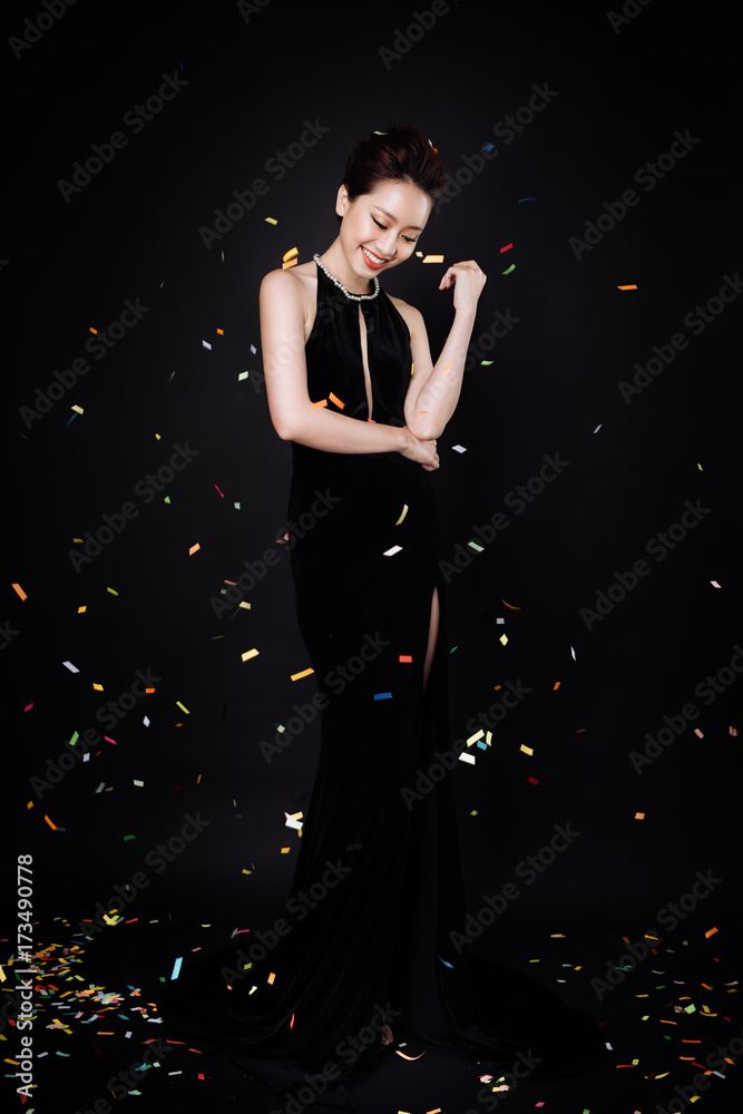 亚洲女性，化着时尚的妆，穿着奢华的黑色连衣裙，五彩纸屑落在她身上。