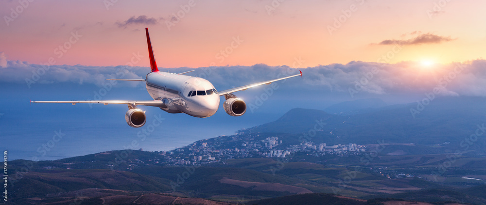 客机。白色飞机的风景在橙色的天空中飞行，山上乌云密布
