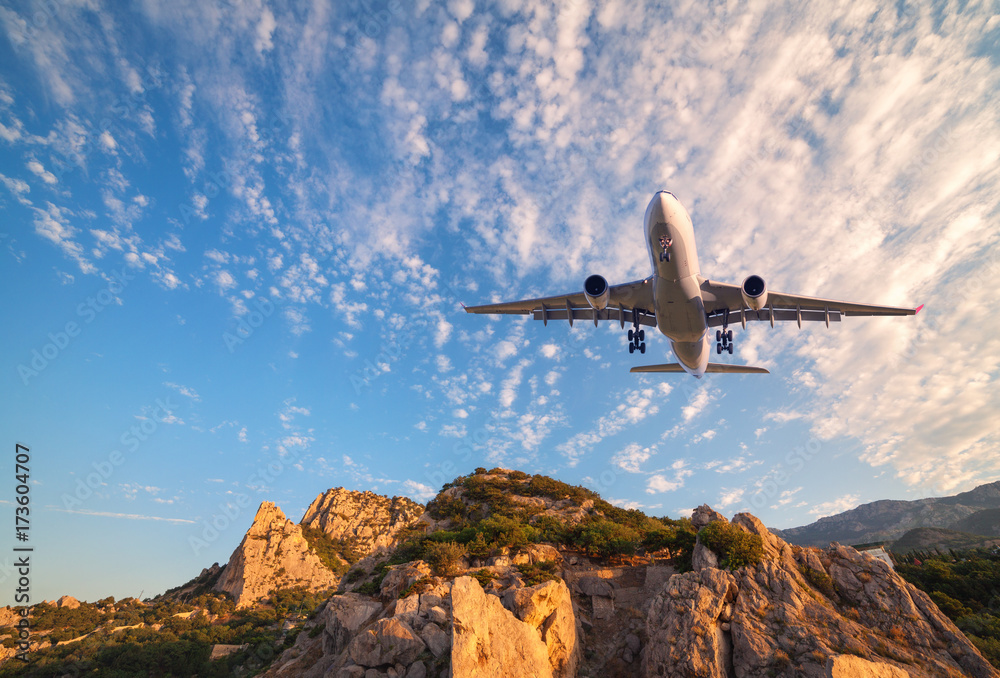 日出时，一架白色的大飞机在岩石上飞行。风景如画，有客机，有山脉，等等。