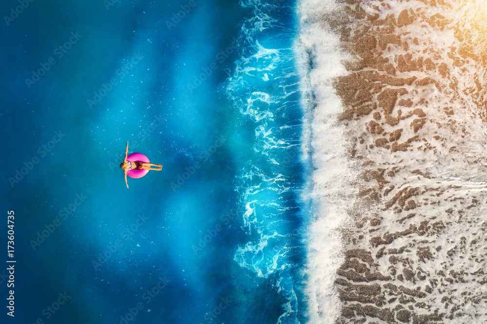 Aerial view of young woman swimming on the pink swim ring in the transparent turquoise sea in Oluden