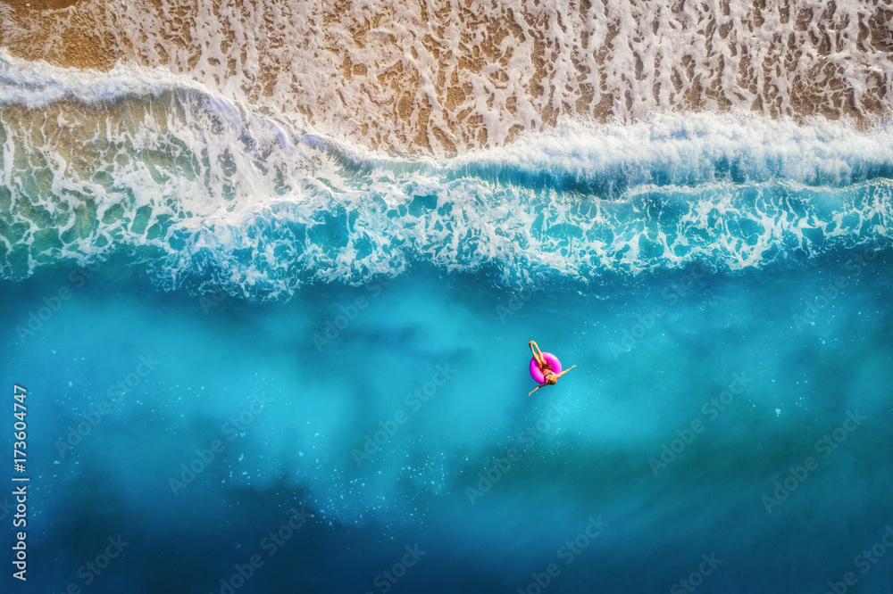 奥卢迪尼透明绿松石海中，苗条女子在粉色游泳圈上游泳的鸟瞰图