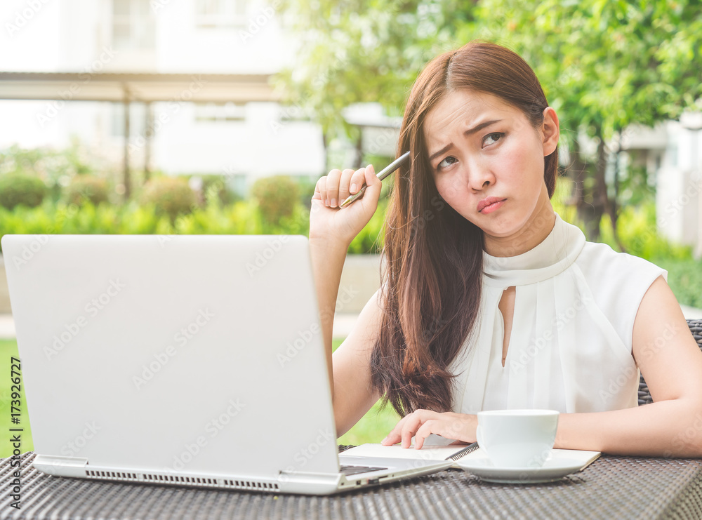 年轻漂亮的亚洲女人在户外公园用笔记本电脑/互联网/网上购物，思考f