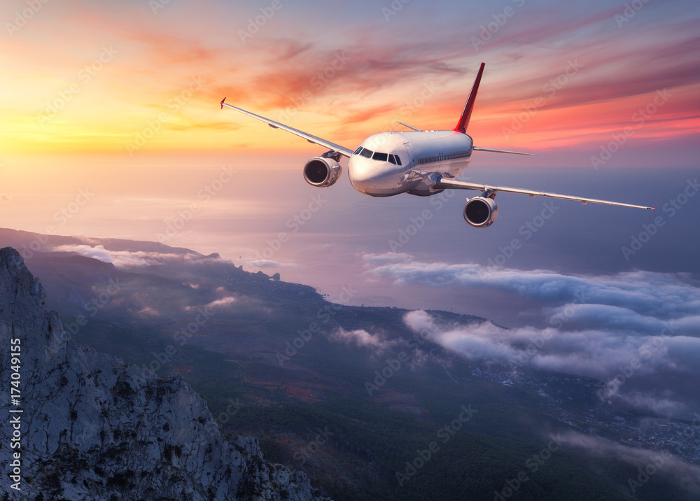 日落时，飞机在低云上飞行。风景有客机、山脉、大海和
