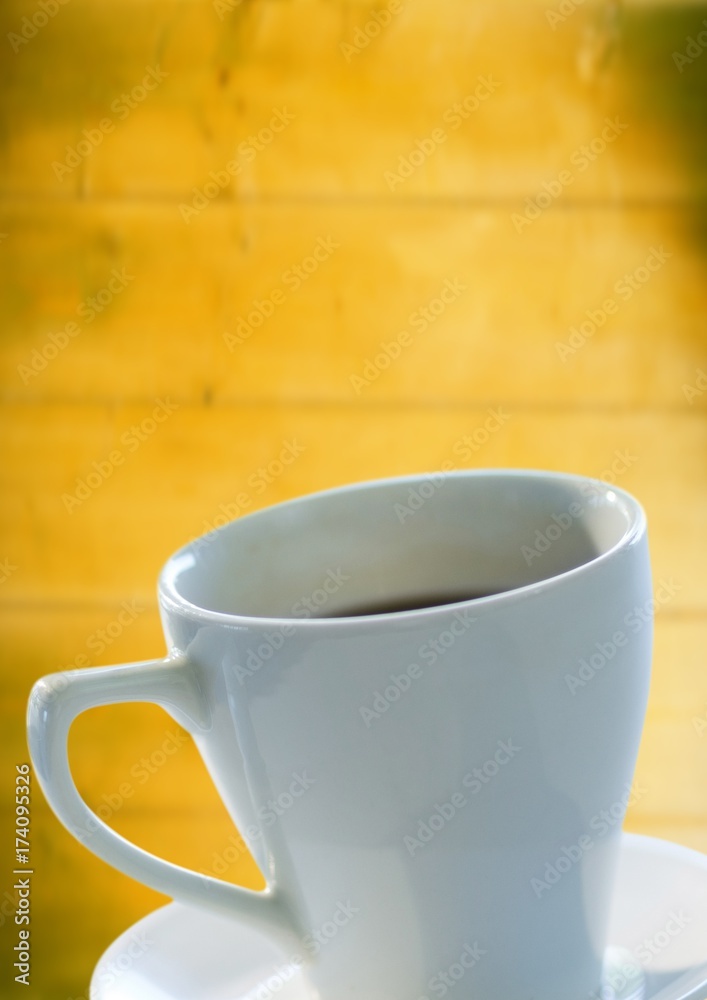 白色咖啡杯和茶托靠着模糊的黄色木板