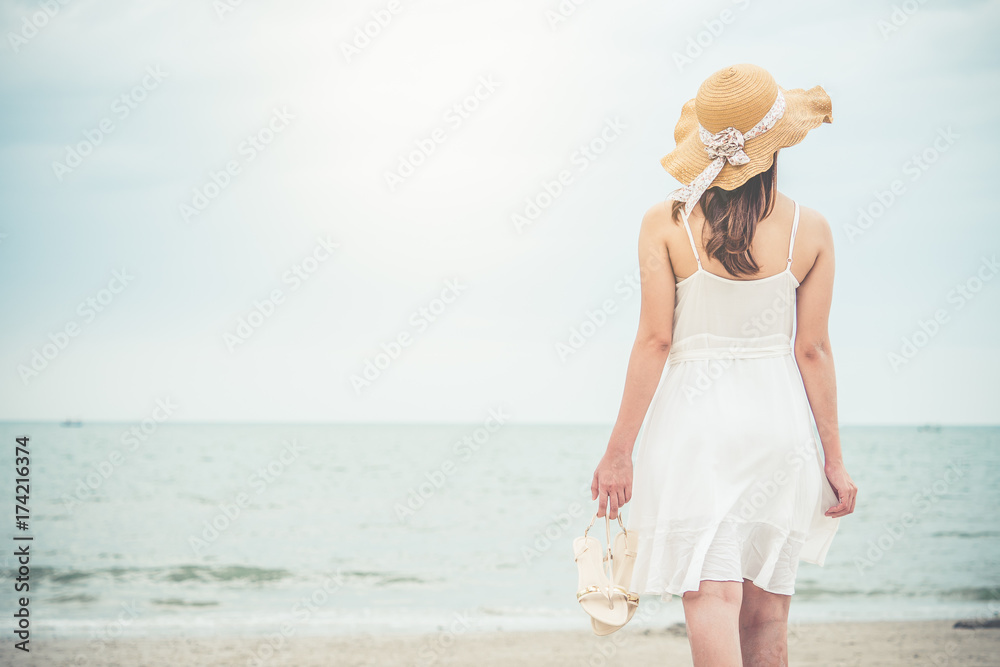 身穿白色连衣裙的亚洲女性站在蓝色的海天之上，在度假时感到放松和快乐