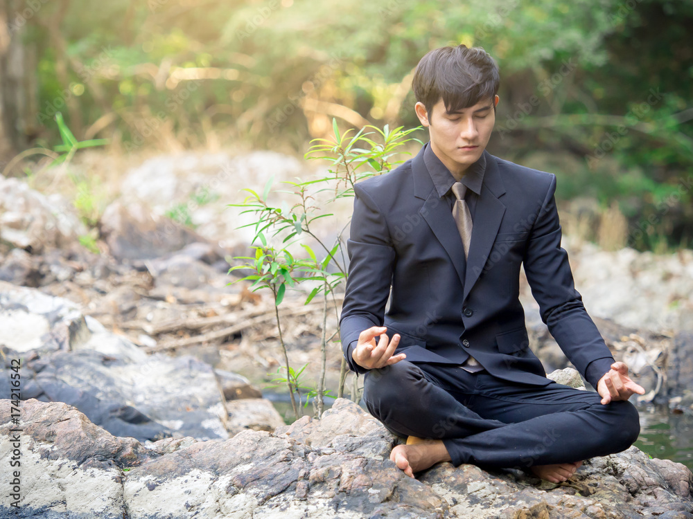 Young asian handsome businessman doing yoga in nature forest for relaxing and meditaing at park outd