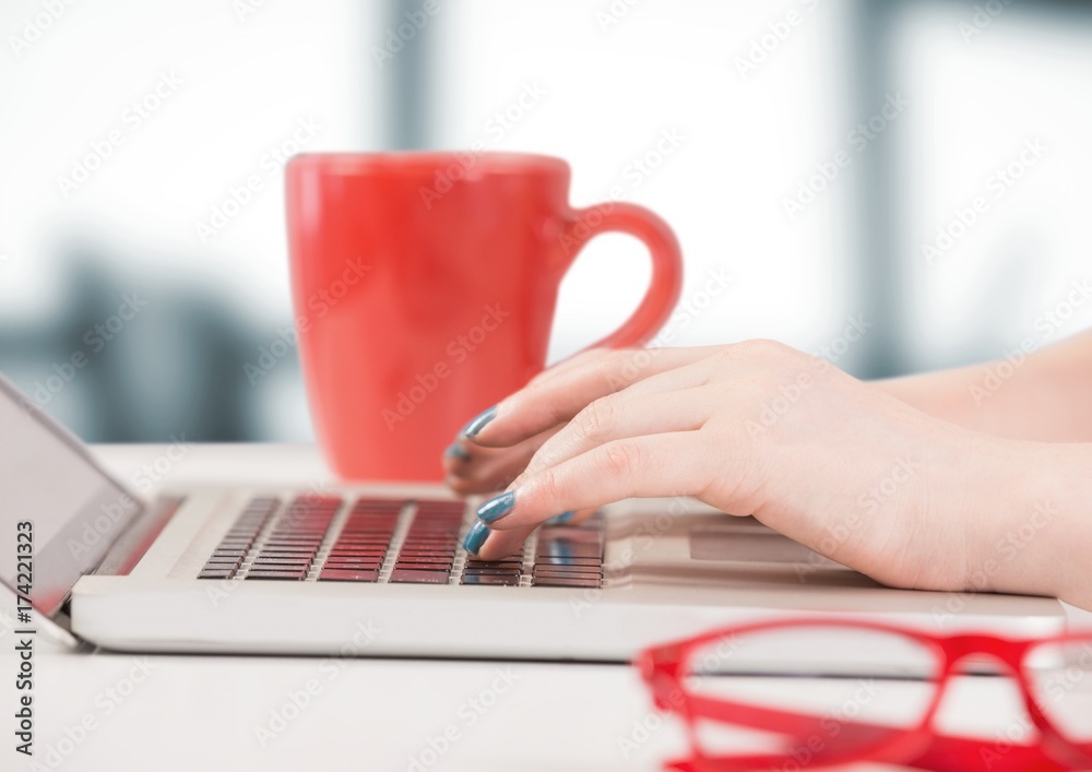 手拿笔记本电脑和红色咖啡杯，对着模糊的灰色办公室