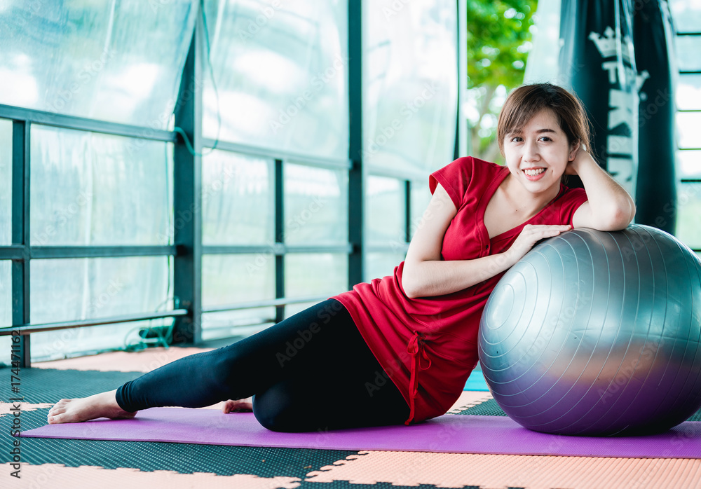 Asian teenage girl exercises with a fitness ball in the fitness center with happiness.
