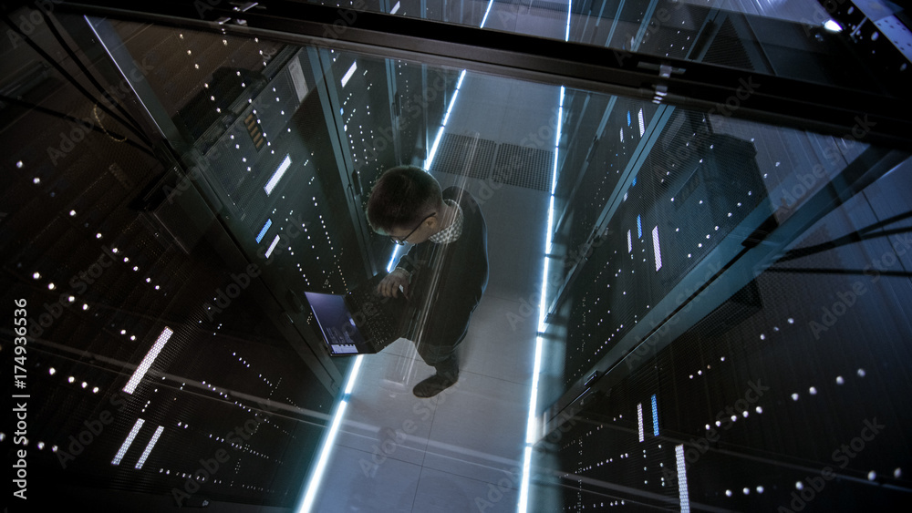 IT工程师在充满有源机架的数据中心使用笔记本电脑的玻璃俯视图