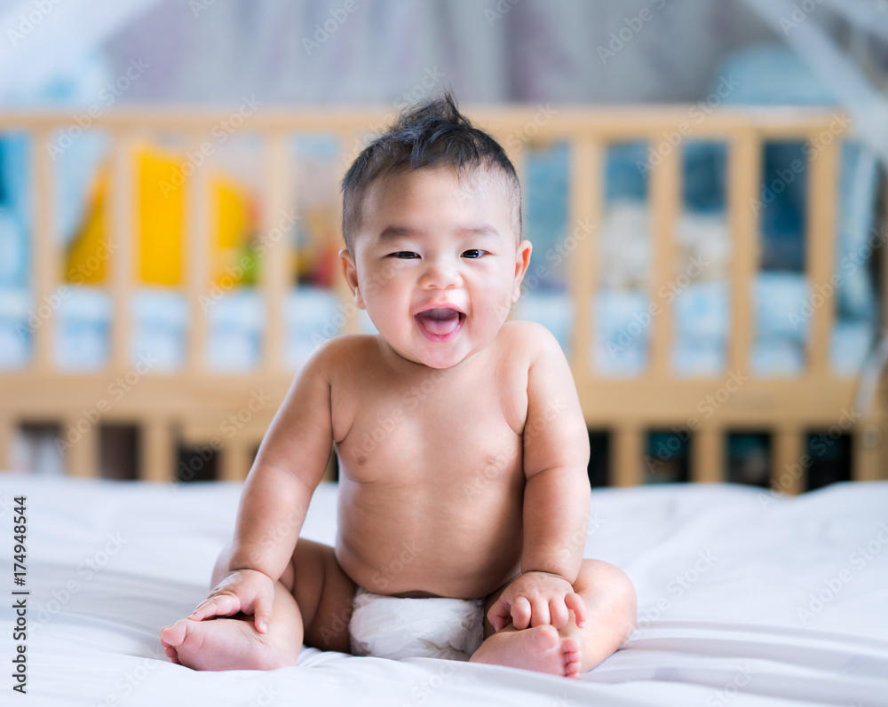 亚洲新生儿坐在卧室的白色床上微笑