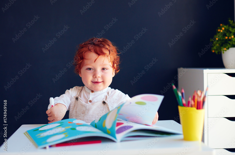 快乐的红发男婴在桌子上的显影书中画画