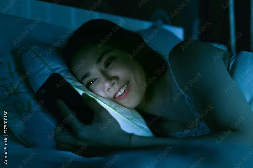 亚洲女人深夜躺在床上用手机发短信，累得睡着了。