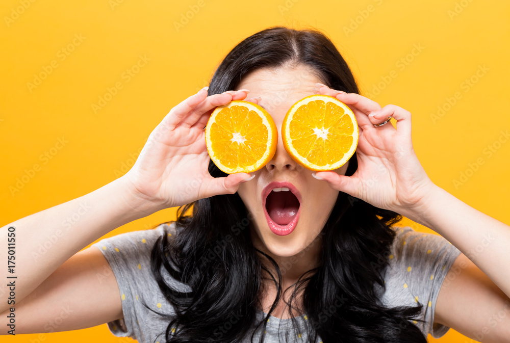 黄色背景下拿着橘子的快乐年轻女人