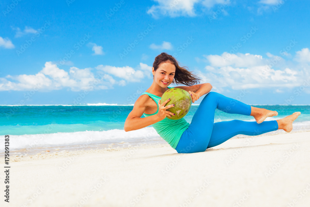年轻女性在海滩上进行腹部锻炼，以保持健康。做仰卧起坐、抬腿