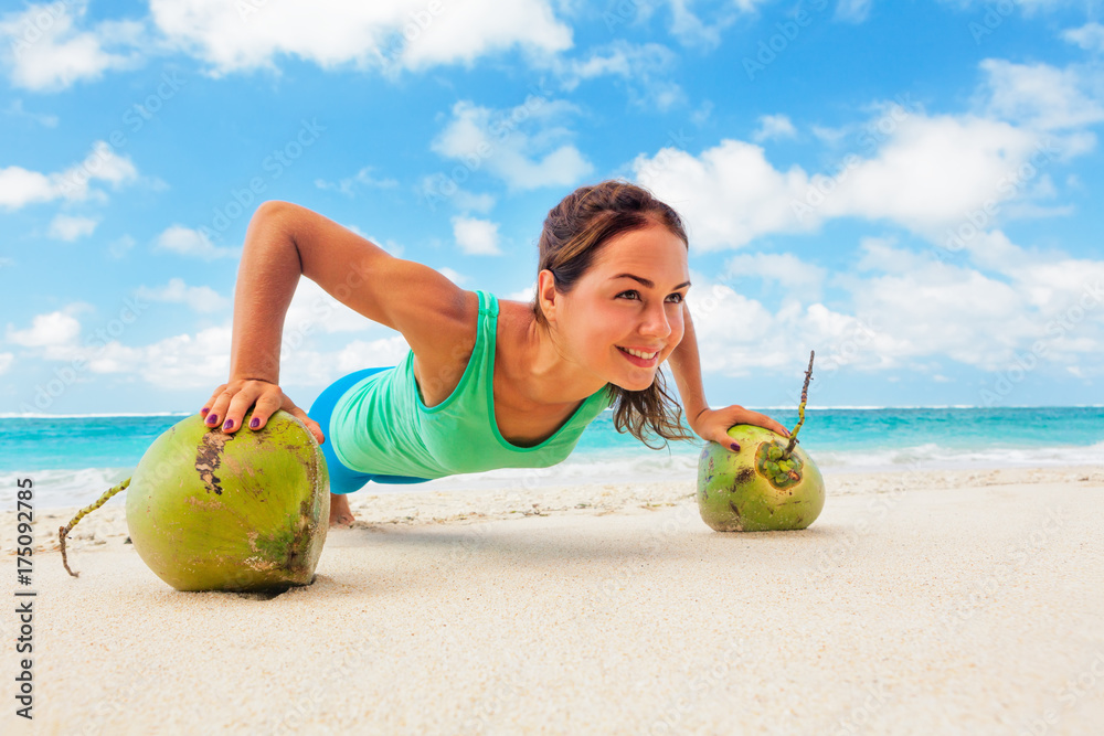 活跃的女性在椰子上做健身运动平板，以保持健康。海滩冲浪背景。