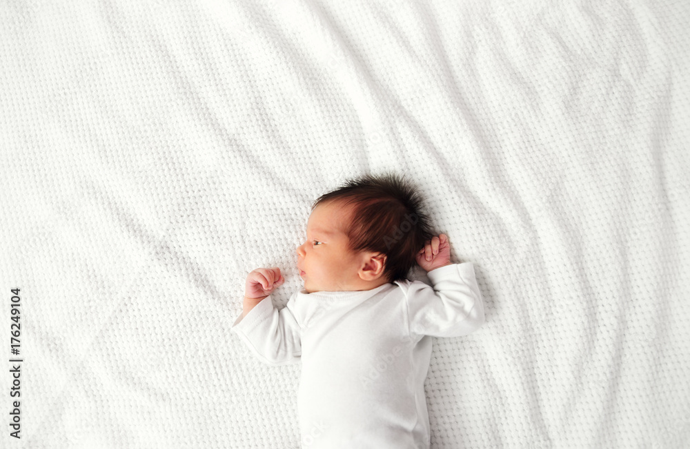 可爱的新生女婴躺在床上。两周大的婴儿躺在白色柔软的毯子上