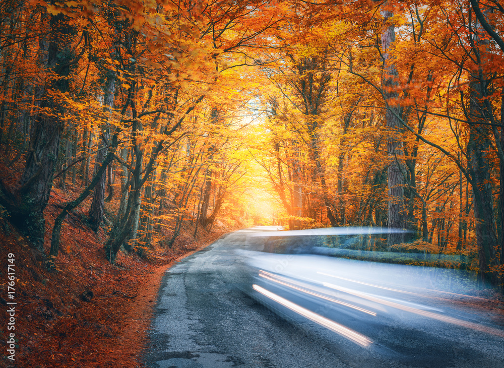 日落时，秋天森林里的山路上有一辆模糊的汽车。晚上汽车在行驶。太美了