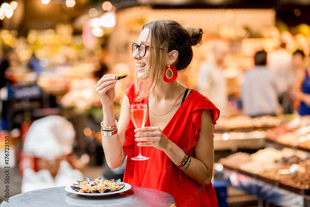 一位身穿红色连衣裙的年轻女士坐在食品市场上与贻贝和玫瑰酒共进午餐